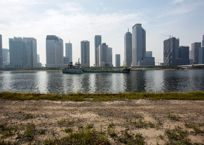 A boat passes in front of the largely desolate Yujiapu Financial District. - Tianjin