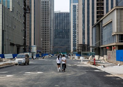 A couple walks down a street of empty office towers in the Yujiapu Financial District. - Tianjin