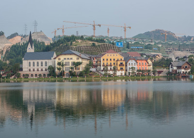 An exact replica of Halstatt, a UNESCO world heritage site in Austria, sits below a hill of cranes on a man-made lake. - Huizhou, Guangdong